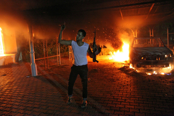 2012年9月11日晚，在班加西美國領事館大院內起火後，建築物和汽車被火焰吞沒，一名武裝人員揮舞著步槍。