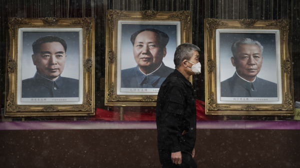 2020年2月14日，在一家几乎无人的北京商场前，一个人戴着口罩走过毛泽东、刘少奇和周恩来的画像。