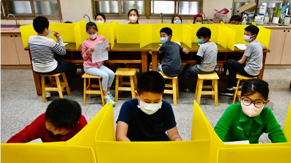台北大甲小学的学生们在带塑料隔板的桌子上吃午餐，以防遏制武汉肺炎病毒的蔓延。