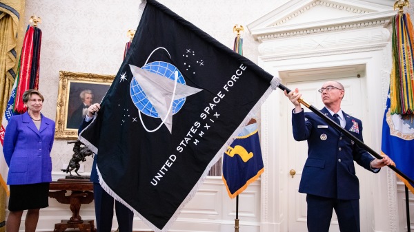 在白宫椭圆形办公室，空军部长芭芭拉·巴雷特(左)注视着总军士长罗杰·陶伯曼展示美国太空军的军旗。