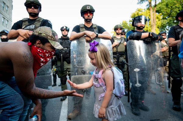 2020年6月3日，华盛顿特区在通向白宫的街道进行的抗议活动上，一名29岁黑人男子与3岁白人女孩米凯拉在警察人墙前拍手。