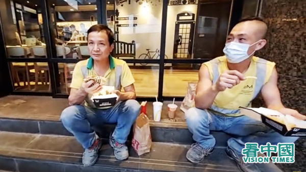 工人黃先生（左）坐在餐廳門外樓梯上吃午飯，自言十分狼狽，還要吃塵吃廢氣。（圖片來源：視頻截圖）