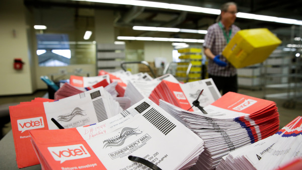 图为堆放在华盛顿州一个邮局桌子上的大量待处理的邮寄选票和紧张工作的邮局人员。（图片来源：JASON REDMOND/AFP via Getty Images）
