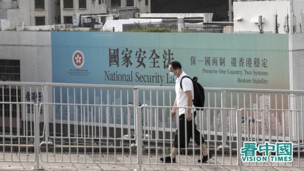  有港人认为国安法彻底摧毁一国两制，纷纷计划移民离开香港。图为一名行人经过国安法宣传牌。（图片来源：庞大卫/看中国）