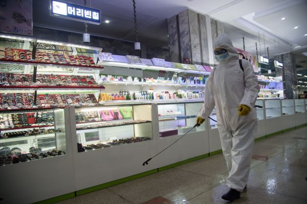12月28日，在平壤第一百货公司开业前，一名卫生工作者在喷洒消毒剂。