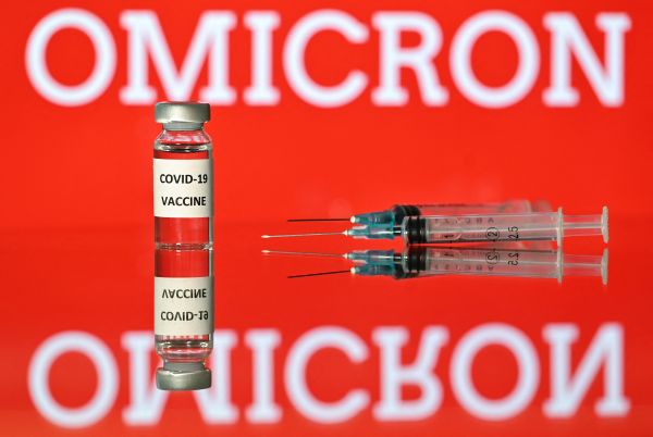 2021 年 12 月 2 日在伦敦拍摄的插图图片显示了一个贴有 Covid-19 疫苗贴纸的小瓶，旁边是注射器和一个屏幕，屏幕上显示了“Omicron”这个词，这是新的 covid 19 变体的名称。