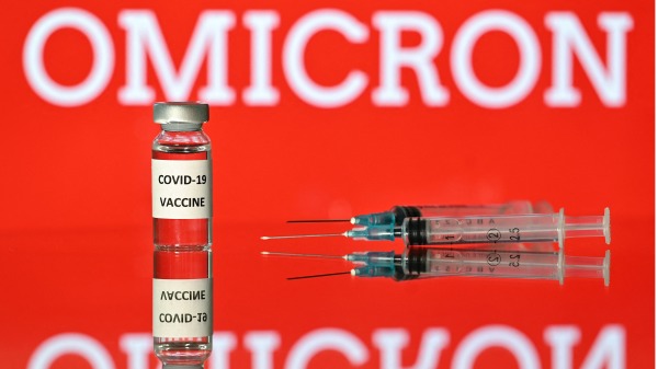 2021 年 12 月 2 日在倫敦拍攝的插圖圖片顯示了一個貼有 Covid-19 疫苗貼紙的小瓶，旁邊是注射器和一個螢幕，螢幕上顯示了“Omicron”。