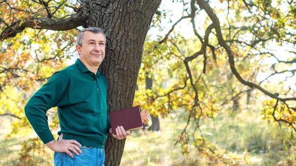 一個男人拿書站在樹下
