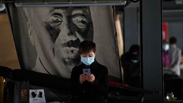 2021年4月25日，在北京潘家园旧货市场，一位女士在一副毛泽东画像前看手机。
