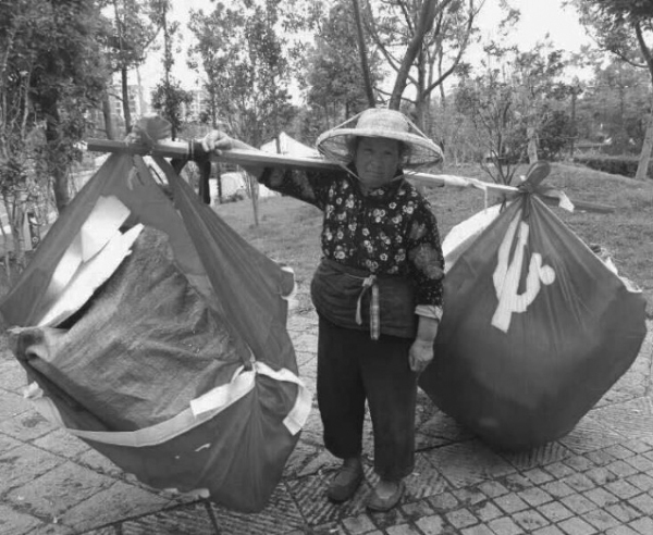 一位中國大娘挑着用破舊的中共黨旗裹着的回收品