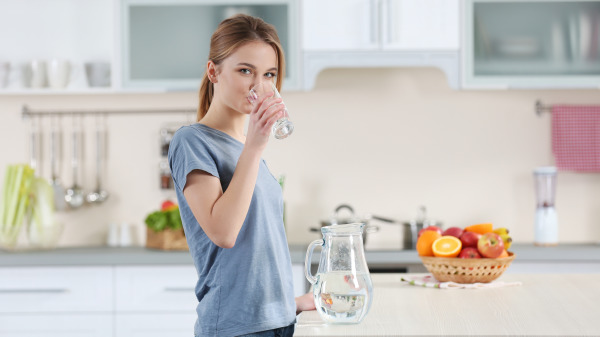 女人站在桌边拿着一杯水在喝