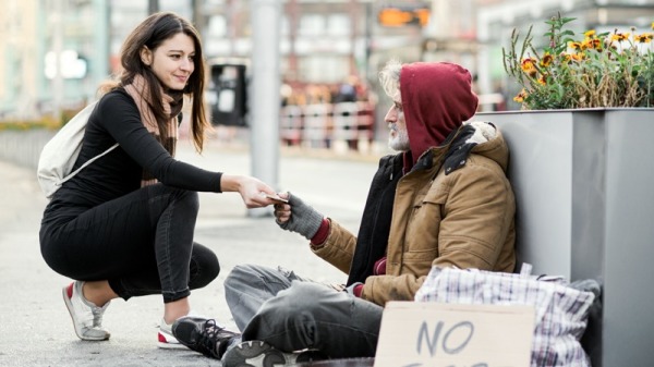 年轻女人把钱给无家可归的乞丐。