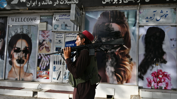 2021年8月18日，在阿富汗首都喀布尔，一名塔利班战士走过一家美容院，店面外面的大幅女性广告照片已经被喷漆涂污。（图片来源：WAKIL KOHSARAFP via Getty Images）