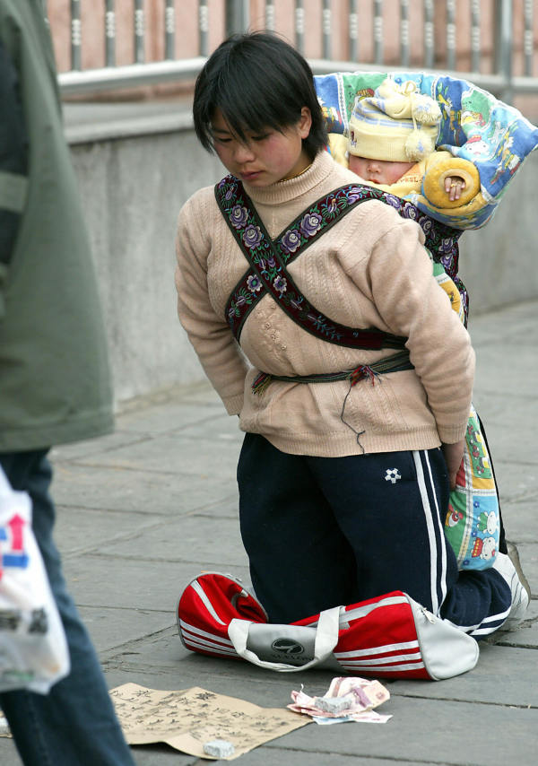 北京，由于失业，一名背着孩子的中国农民工妇女跪在购物中心外，乞求路人给零钱。