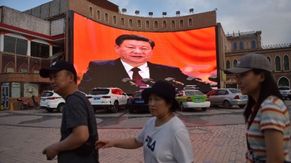 2019年6月4日，新疆喀什市的人們走過一個顯示中國國家主席習近平照片的大屏幕前。（圖片來源：GREG BAKER/AFP/Getty Images）