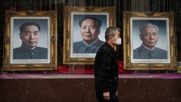 2020年2月14日，在一家幾乎無人的北京商場前，一個人戴著口罩走過毛澤東、劉少奇和周恩來的畫像。