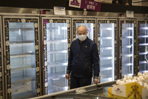 2020年2月12日，武汉市一个超市内，一戴口罩的男子正在购物，他的身后是一排排空货架。