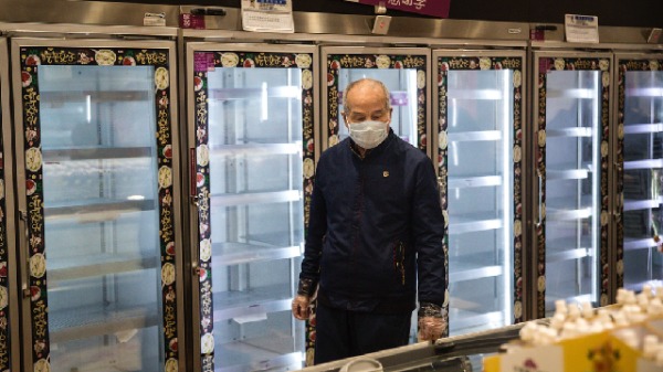 2020年2月12日，武汉市一个超市内，一戴口罩的男子正在购物，他的身后是一排排空货架。