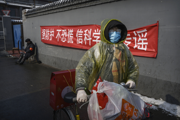 2020年2月07日，北京一名戴着防护口罩、塑料外套和橡胶手套的妇女推着自行车走过一处宣传标语前。