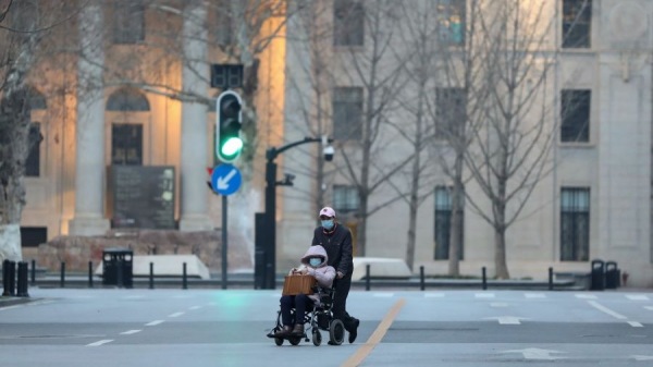 這張攝於2020年3月4日的照片顯示，一名插入口罩的男子穿過武漢市的一條街道推著坐輪椅的人。