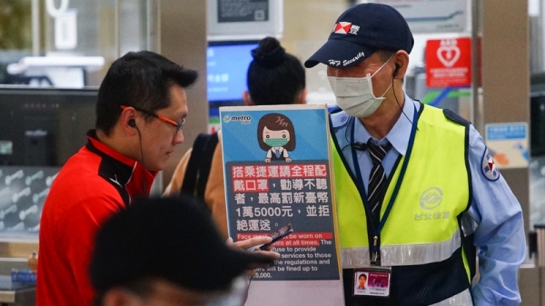 台北捷運站務人員持看板勸導未戴口罩的民眾，希望民眾配合政策規定加強防疫。