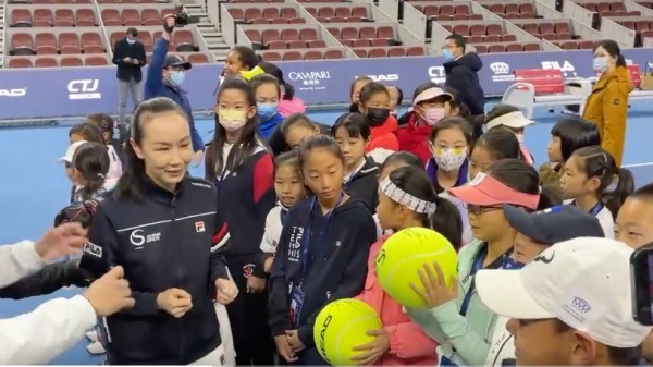 彭帅在消失多日后，21日与体育界官员一起出席北京的青年网球比赛公开活动。照片为彭帅为小运动员手中的超大型网球签名。