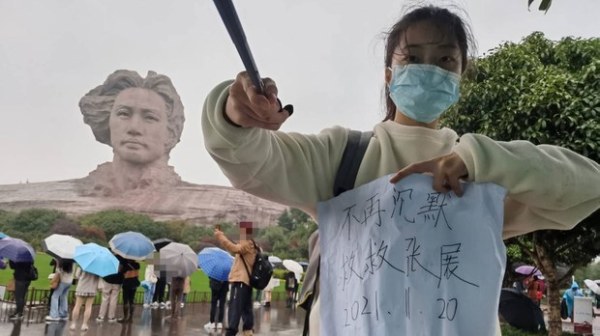 湖南长沙一名大学女生，在当地著名景点橘子洲头举牌声援张展，纸上写着“不再沉默，救救张展”的字句。