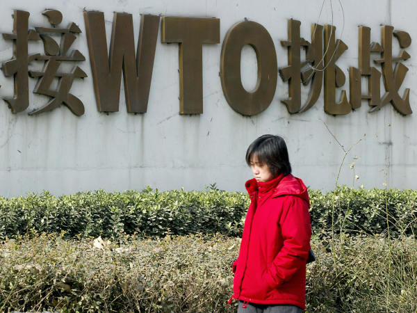 一个中国女子走过一个WTO广告牌前。