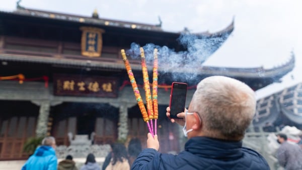 2021年2月16日在上海的一座寺庙祈祷时，一男子上香拍照。