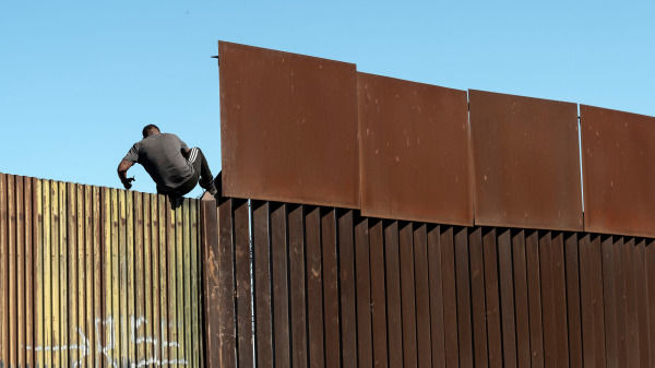 一名男子正试图越过位于加利福尼亚州区域内的美国-墨西哥边境的栅栏进入美国