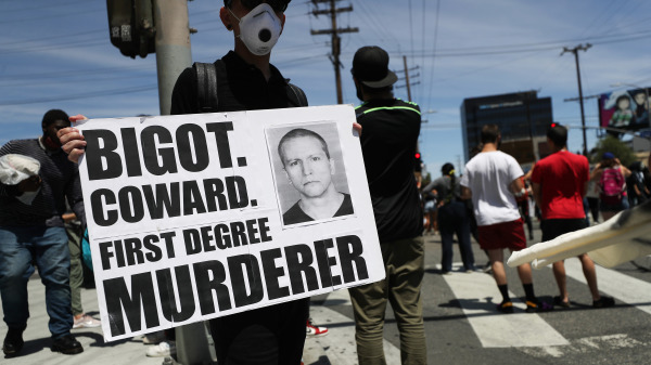 圖為“黑命貴”運動成員對喬治·弗洛伊德（George Floyd）之死舉行抗議活動，示威者手持牌子上的照片是涉案的前警察德里克·沙文（Derek Chauvin）。（圖片來源：Mario Tama/Getty Images）