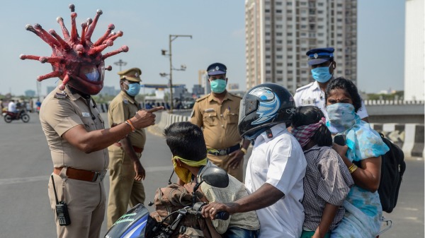 印度钦奈一名警察头戴冠状病毒形状的头盔，在一个检查站与一个骑摩托车民众家人交流。