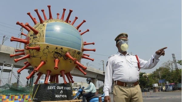 一名印度交通官員站在以冠狀病毒為主題地球儀旁邊，檢查通勤者是否遵守防疫規定。