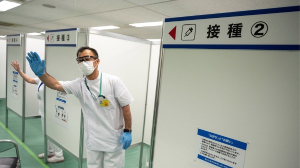 2021年5月21日，日本自卫队在东京接种中心进行Covid-19疫苗接种模拟，一名医务工作人员向参与者招手。
