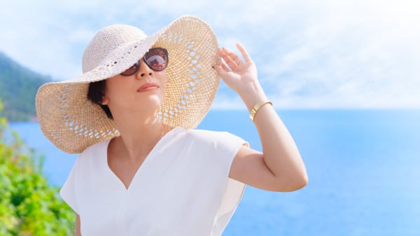 女人戴着太阳眼镜 手碰着遮阳帽 头扬起看着上前方