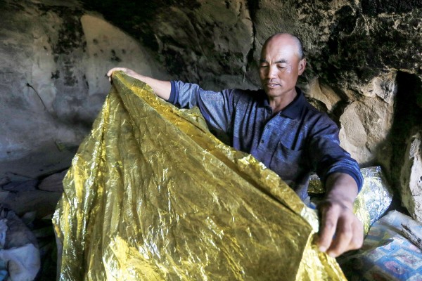 牧羊人朱克明拯救了 6 名超級馬拉松運動員，他在洞穴住宅中，展示了保護受災者的保溫毯。