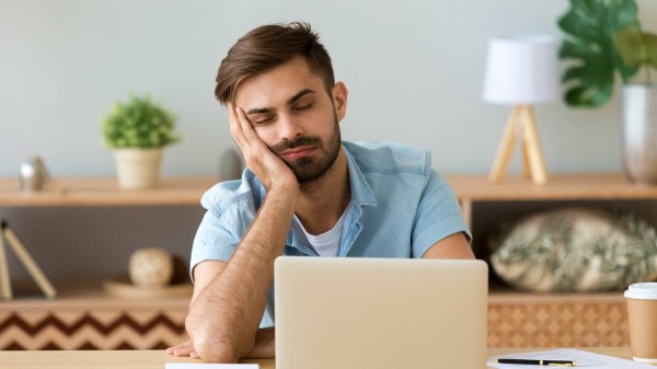 一个男人工作很累，桌上有电脑和咖啡
