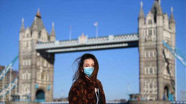 一名戴口罩的女士在英国伦敦塔桥前合影留念。