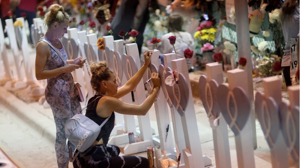 2021年7月15日，人们在佛州公寓倒塌遇难者纪念墙前悼念。（图片来源： Joe Raedle/Getty Images）