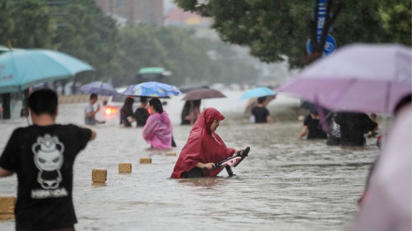 2021年7月20日，中国河南省郑州市人们在暴雨中涉水走过街道。