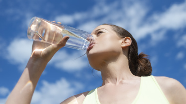 一个女人在户外手拿一个喝保特瓶水在喝水