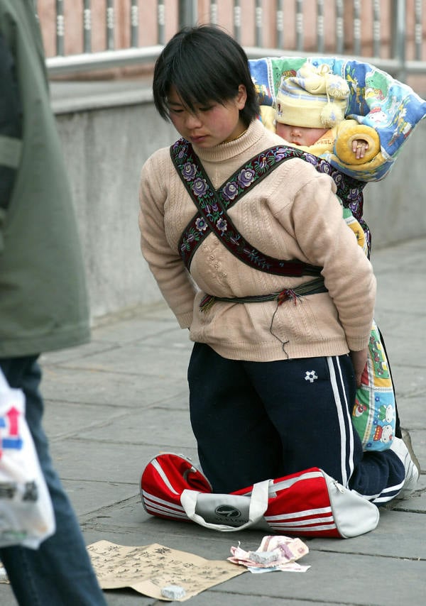 北京，由于失業，一名背著孩子的中國農民工婦女跪在購物中心外，乞求路人給零錢。